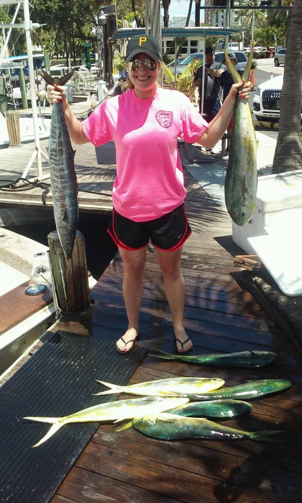 Fisher gal holding a wahoo and dolphin and more dolphin laying at her feet at the dock