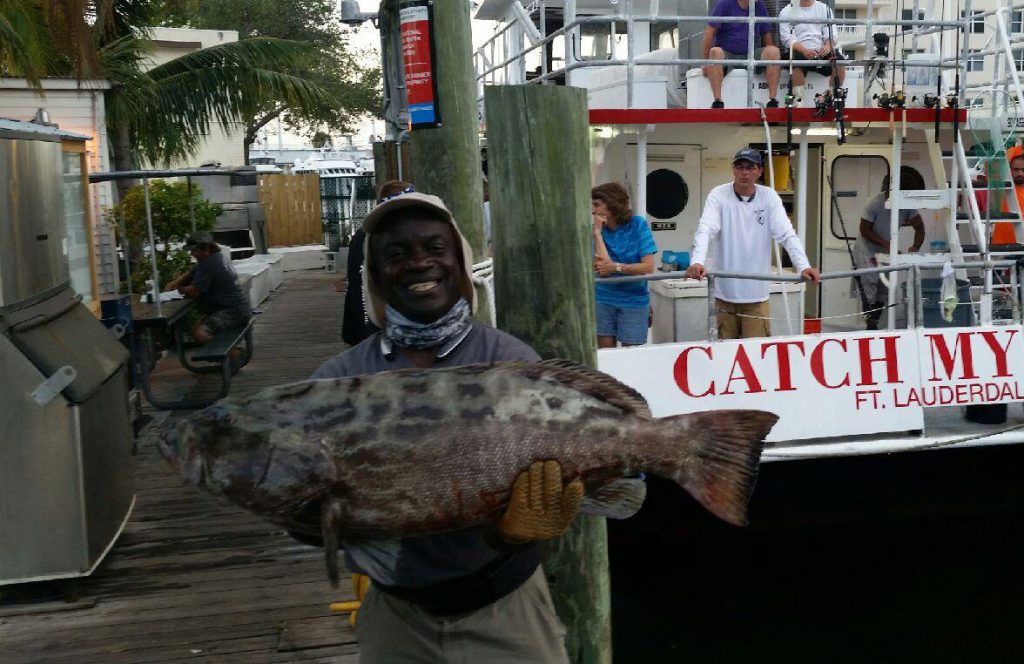 Leslie holding a monster black grouper behind the Catch My Drift