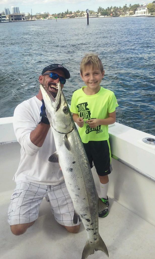 Kid with a giant barracuda in the boat.
