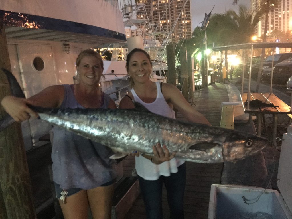 2 girls holding their huge kingfish at the dock for a photo. Probably a 65 pound kingfish!