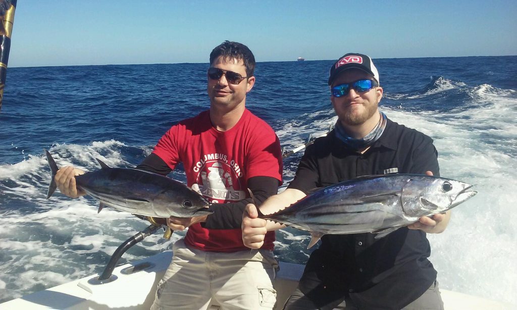 2 guys holding tunas freshly caught on a fishing charter