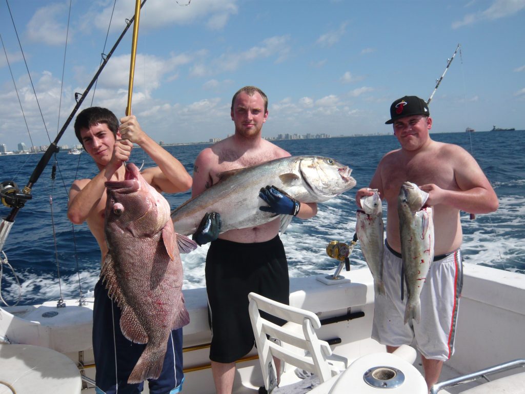 3 guys at sea in a boat holding up a big grouper, amberjack and some tilefish.