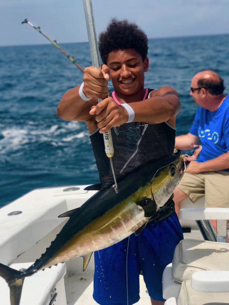 Teenager holding a blackfin tuna on the gaff freshly brought out of the water.