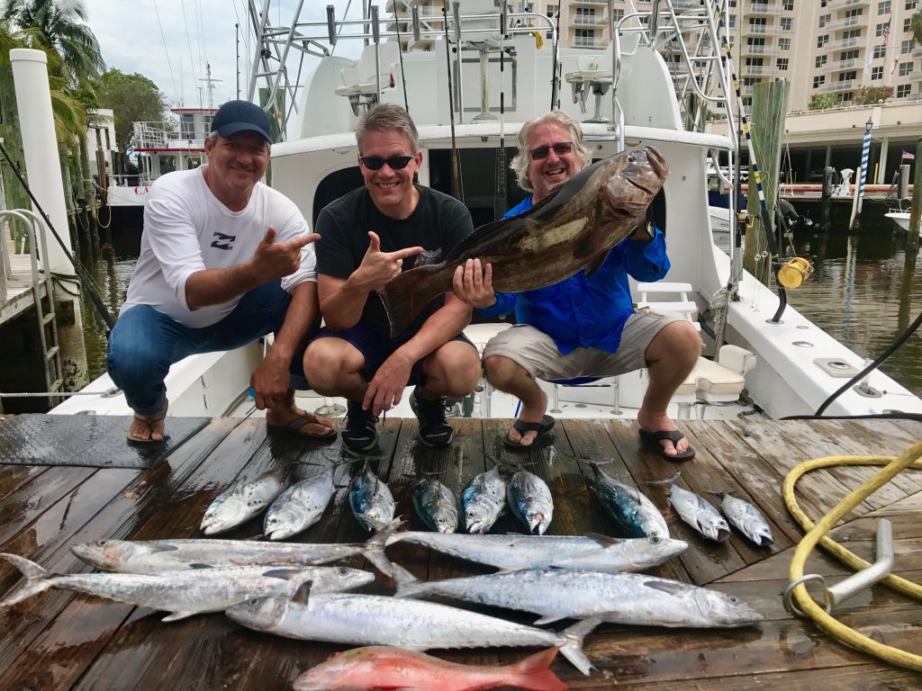 3 guys kneeling next to their mixed bag of fish they came back in with on a charter