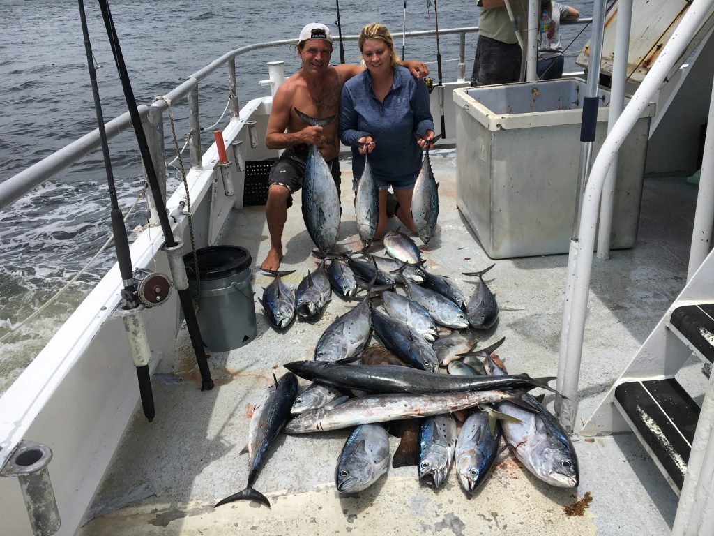 Ashley and Justin kneeling on deck with a big pile of bonitos laying on the deck of the boat.