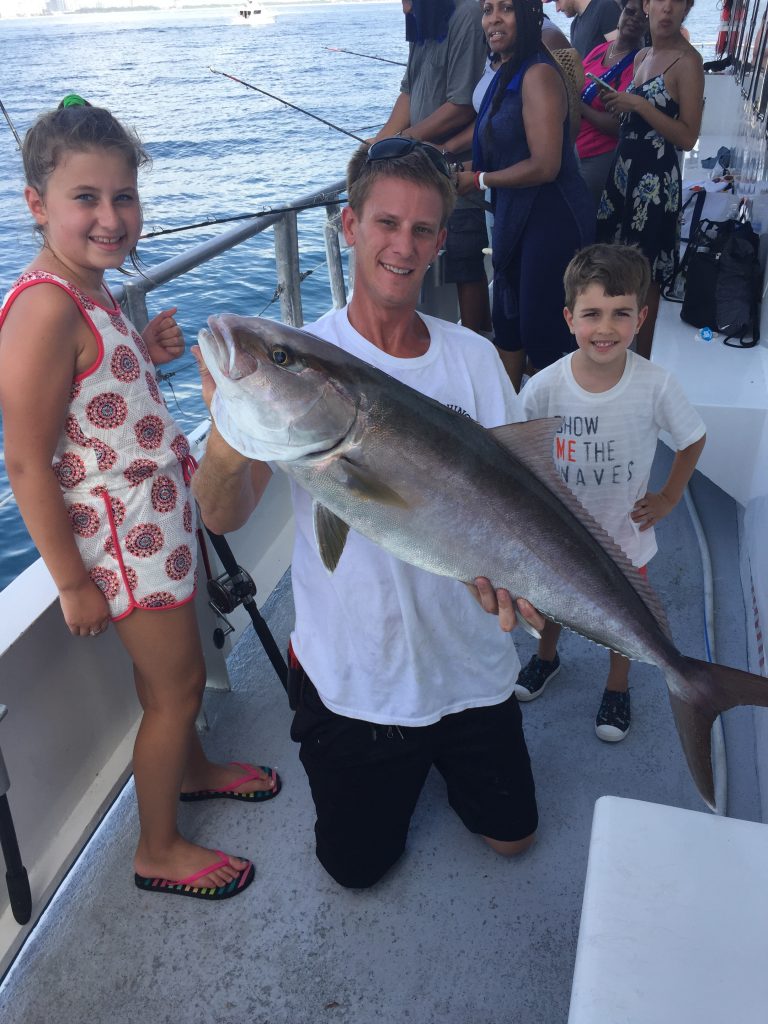 Capt Chris holding a big amberjack next to the 2 kids who caught it on the boat.
