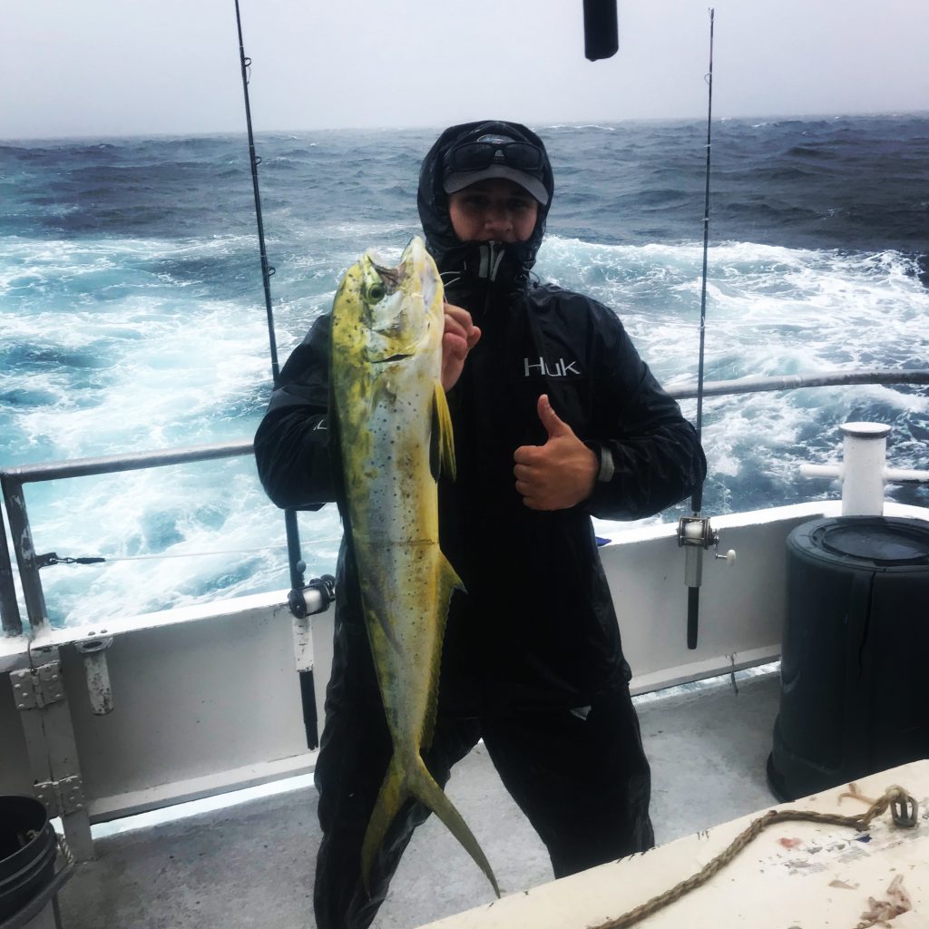 Evan in full rain jacket holding a dolphin he just caught aboard the Catch My Drift.