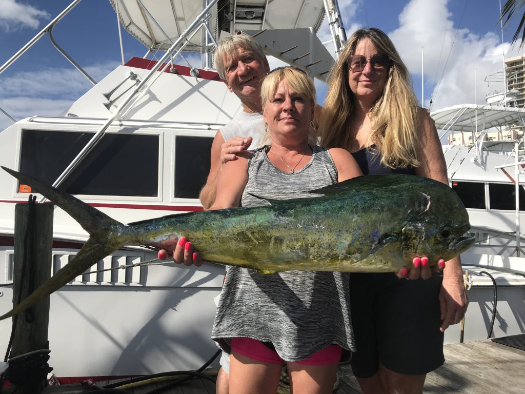 3 folks at the dock, holding up a nice bull dolphin they just caught on their fishing charter.