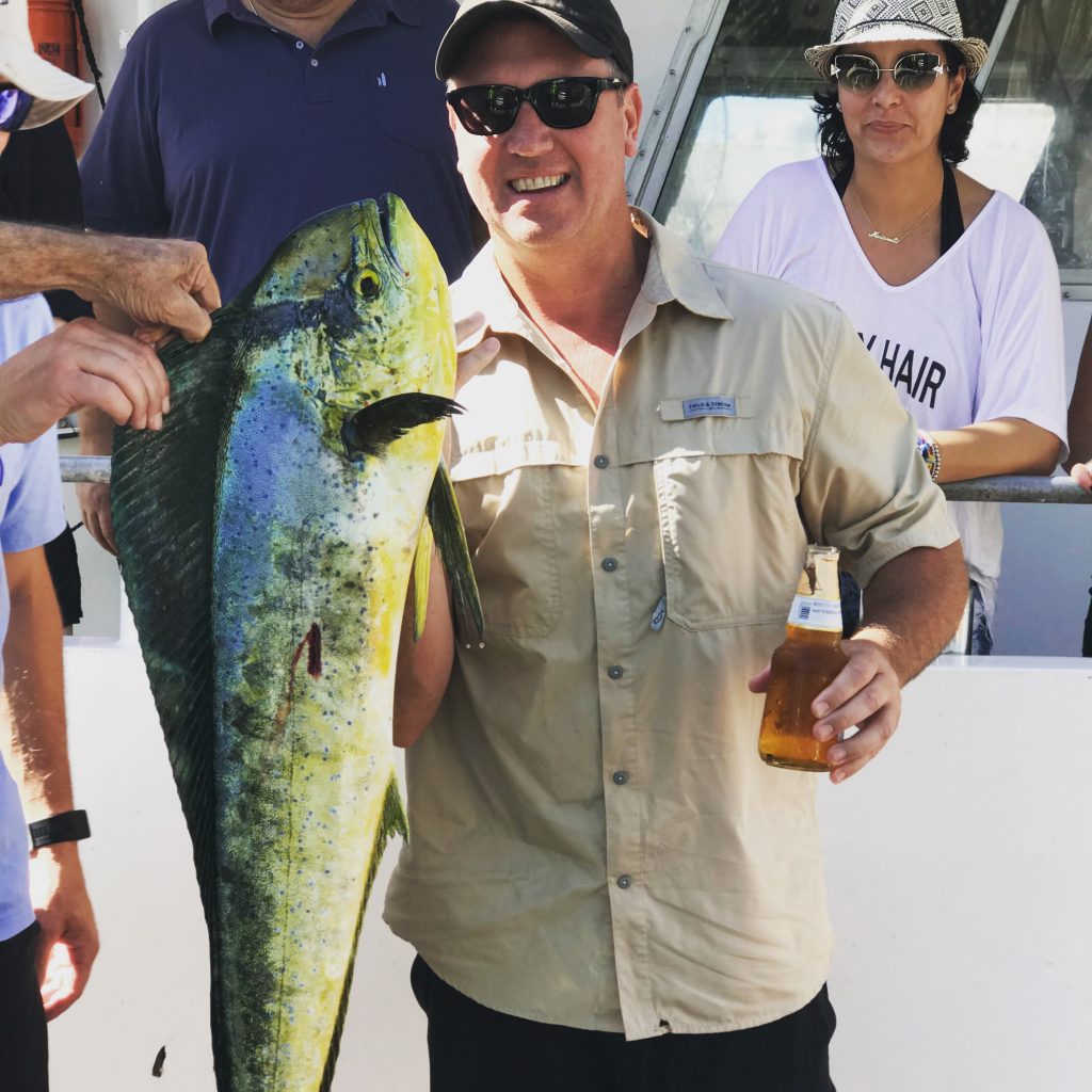 Nice dolphin being held at the dock by a happy angler with his coworkers behind him posing for a picture.