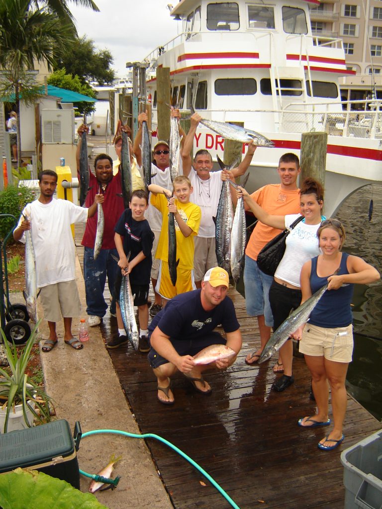 Folks on a party boat fishing trip holding their catch at the dock.