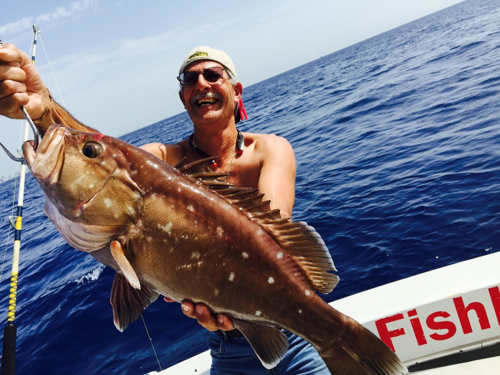 Happy fisherman posing with a snowy grouper