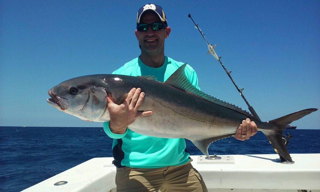 Exhausted angler holding a big amberjack just brought up from the deep