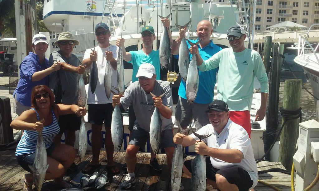 Group of people holding their catch of bonitos and kingfish at the dock after their trip.