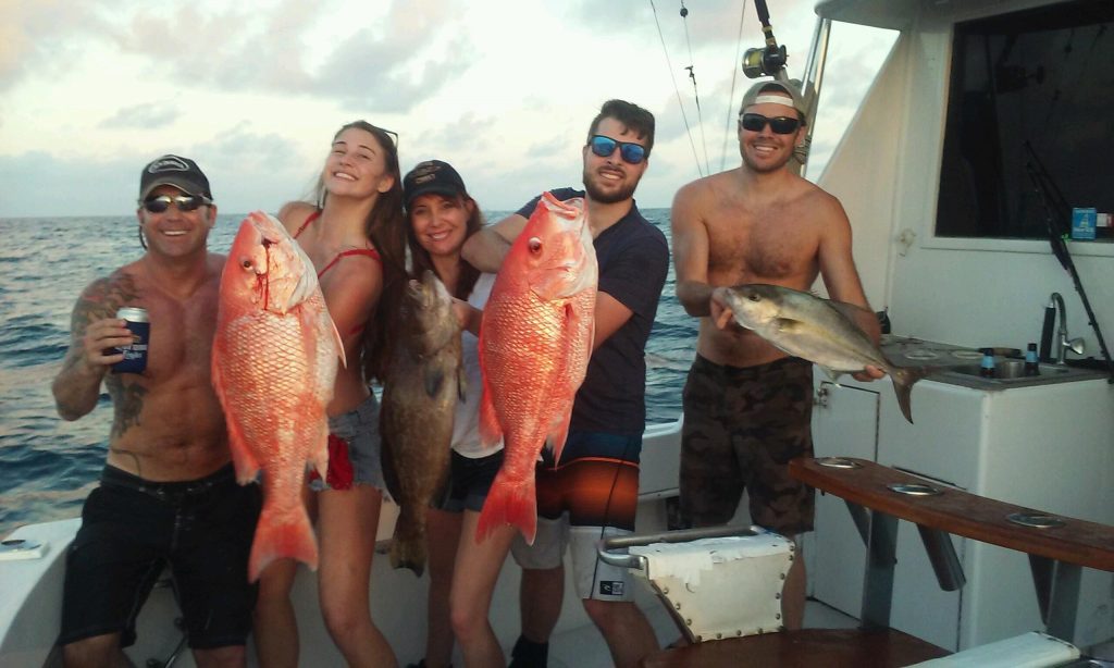 Happy anglers holding a couple huge red snappers and a big grouper