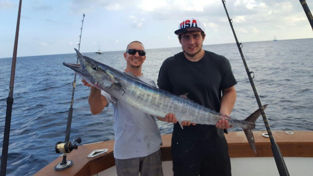 2 guys holding a big wahoo on the boat on a calm day at sea