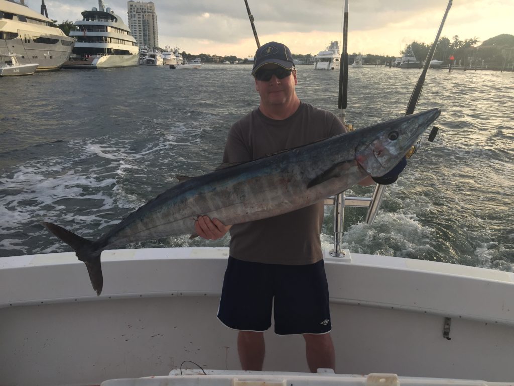 Guy holding a wahoo with the sunset in the background.