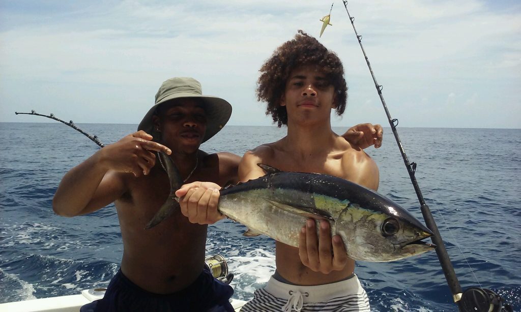 2 guys on a boat in the ocean holding about a 12 pound blackfin tuna they just caught.