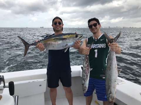 A couple guys holding their catch of a blackfin tuna and 2 nice kingfish, on a boat while out in the ocean.