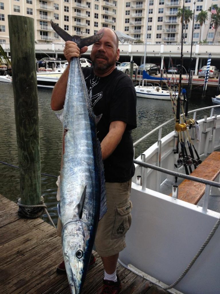 Guy holding a big wahoo at the dock next to the Mary B III.