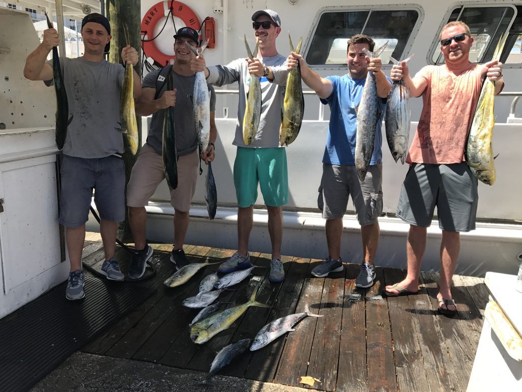 Group of guys on a bachelor party on the dock after a fishing trip holding kingfish, dolphin and tunas.