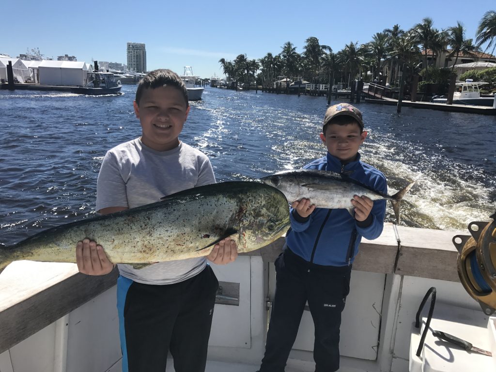 2 boys each holding a nice size dolphin fish and a tuna aboard the boat driving through Ft Lauderdale