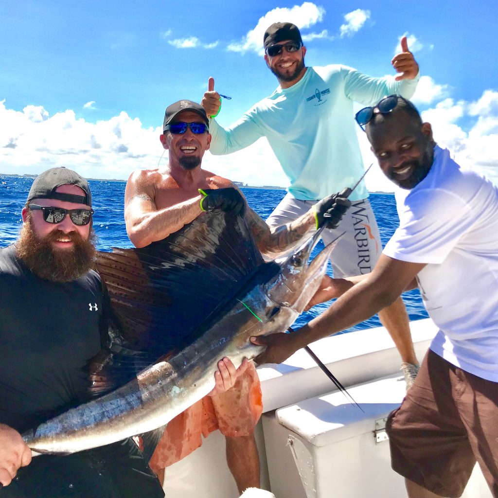 Couple happy anglers posing with a sailfish they just caught, Capt Bobby with thumbs up behind everyone.