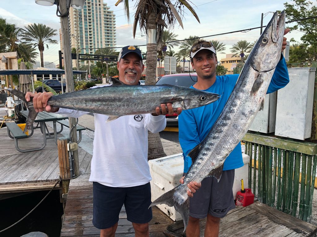 Father and son pose at the dock with a big kingfish and barracuda they just caught on their fishing charter.