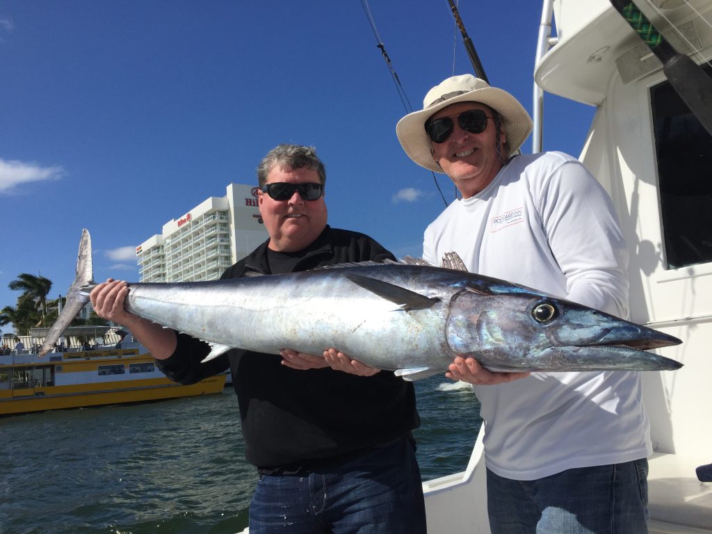 2 happy anglers aboard the boat with a nice wahoo they just caught on their fishing charter.