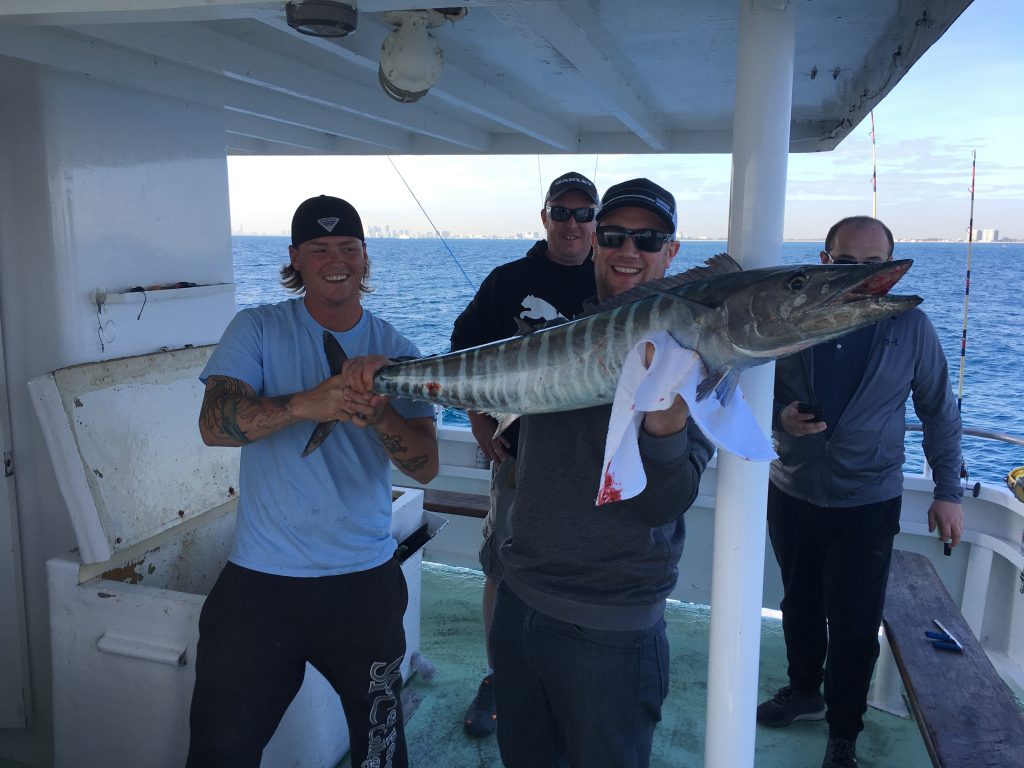 Group of bachelor party guys taking a pic aboard the boat with a wahoo they just caught.