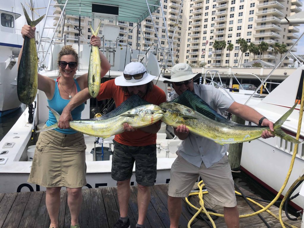 3 people at the dock after the trip holding up some big mahi-mahi.