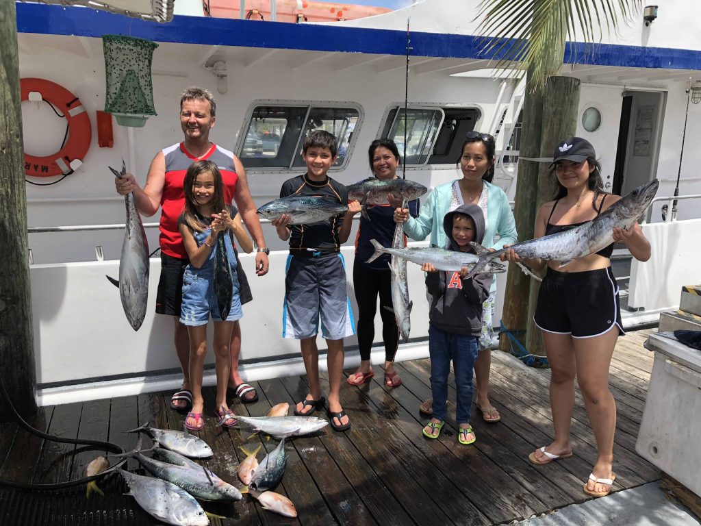 Family at the dock in front of the boat holding their catch of a bunch of fish.