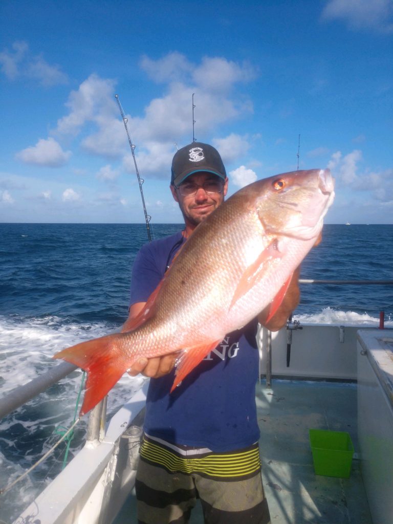 Ryan holding a big mutton snapper he just caught fishing aboard the Catch My Drift with a beautiful ocean and sky in the background.