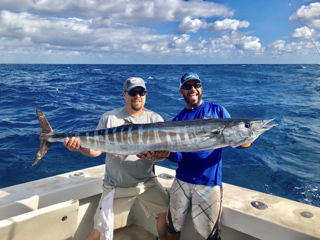 Capt Bobby holding a 50 pound wahoo in the boat with the happy angler who caught it. Beautiful sky in the background amidst a choppy ocean.