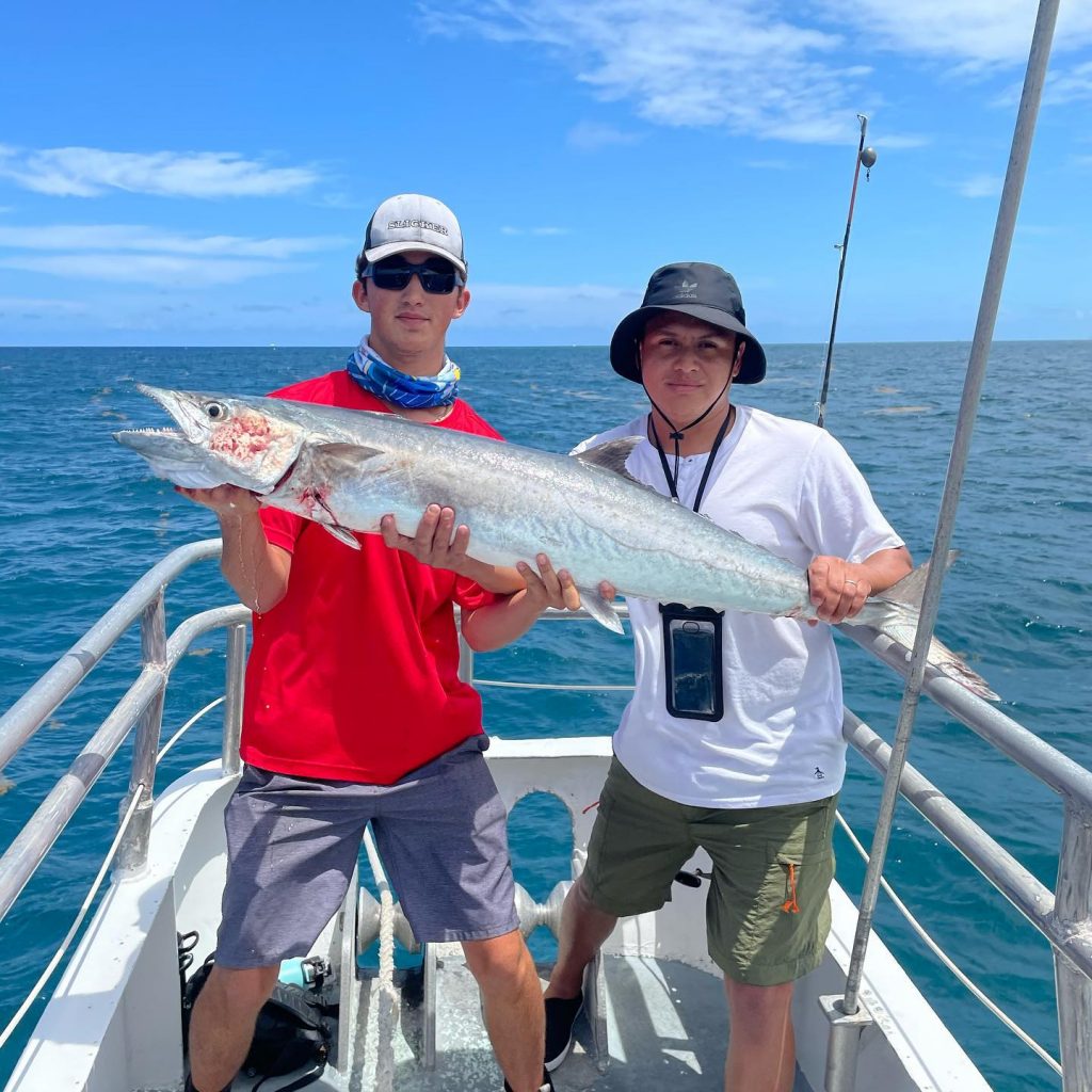 Fabrizion holding a big kingfish on the boat at sea alongside the lucky angler who caught it